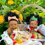 Deux poupées Madin Dolls en robes madras traditionnelles, posées dans un panier fleuri, faites main en Martinique.